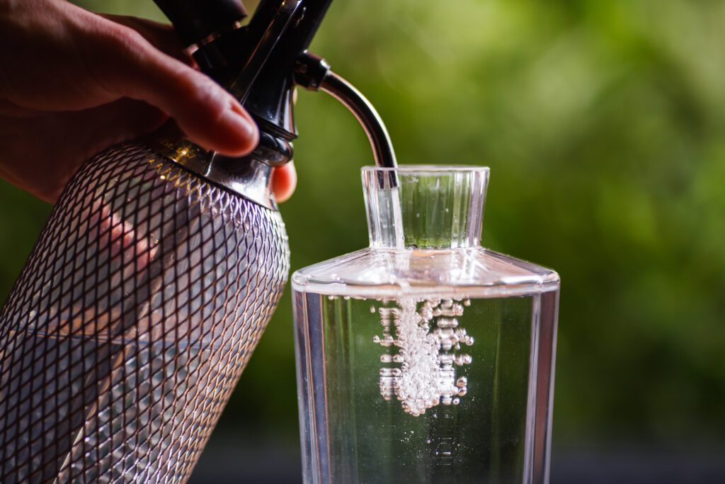 The hand holding the siphon, bubbles with clear water in a glass decanter.